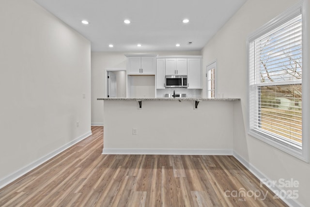 kitchen with white cabinets, a kitchen bar, light hardwood / wood-style floors, kitchen peninsula, and light stone countertops