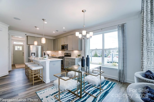 kitchen featuring pendant lighting, appliances with stainless steel finishes, gray cabinetry, backsplash, and an island with sink