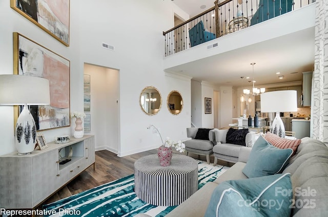 living room with an inviting chandelier, crown molding, dark wood-type flooring, and a high ceiling