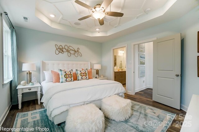 bedroom featuring ceiling fan, ensuite bath, dark hardwood / wood-style floors, and a raised ceiling