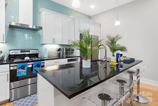 kitchen featuring wall chimney exhaust hood, a kitchen bar, stainless steel electric stove, a kitchen island with sink, and white cabinets