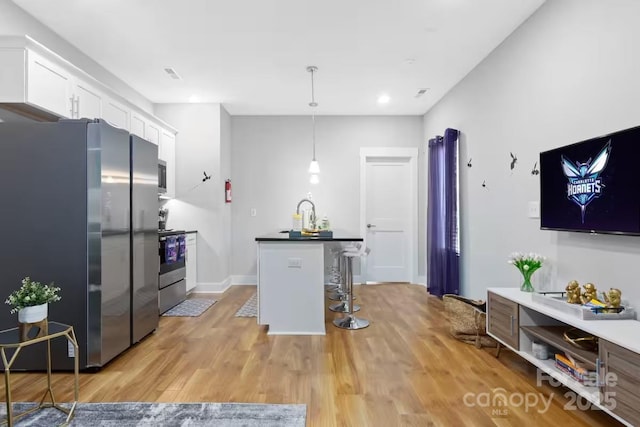 kitchen with appliances with stainless steel finishes, white cabinetry, a kitchen breakfast bar, decorative light fixtures, and light wood-type flooring