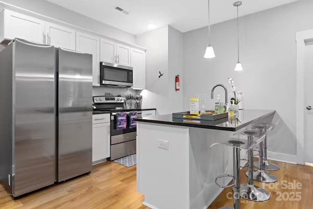 kitchen with a breakfast bar, pendant lighting, white cabinetry, stainless steel appliances, and light hardwood / wood-style flooring