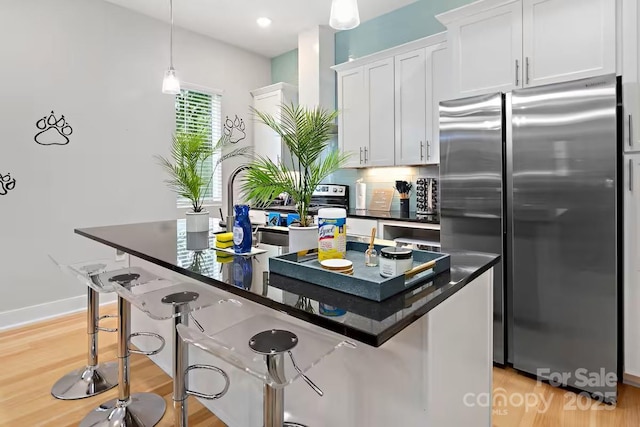 kitchen featuring a breakfast bar, decorative light fixtures, stainless steel fridge, an island with sink, and white cabinets