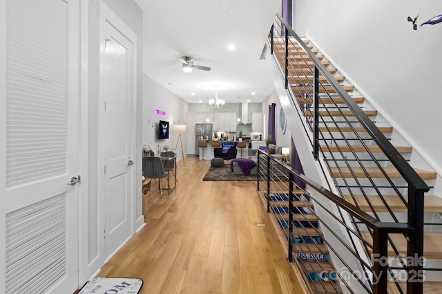 staircase with ceiling fan with notable chandelier and hardwood / wood-style floors