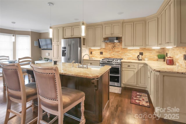 kitchen with pendant lighting, stainless steel appliances, cream cabinetry, and wall chimney exhaust hood