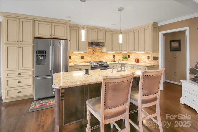 kitchen featuring appliances with stainless steel finishes, hanging light fixtures, ventilation hood, a center island with sink, and cream cabinetry