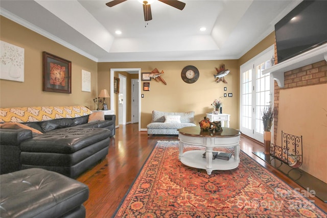 living room with a tray ceiling, dark wood-type flooring, ornamental molding, and ceiling fan