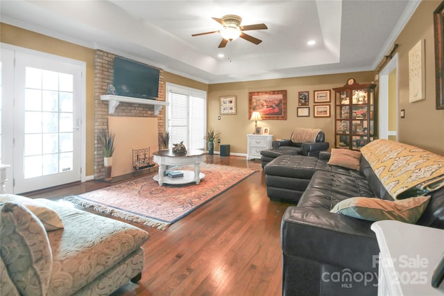 living room with hardwood / wood-style floors, a fireplace, a raised ceiling, and ceiling fan