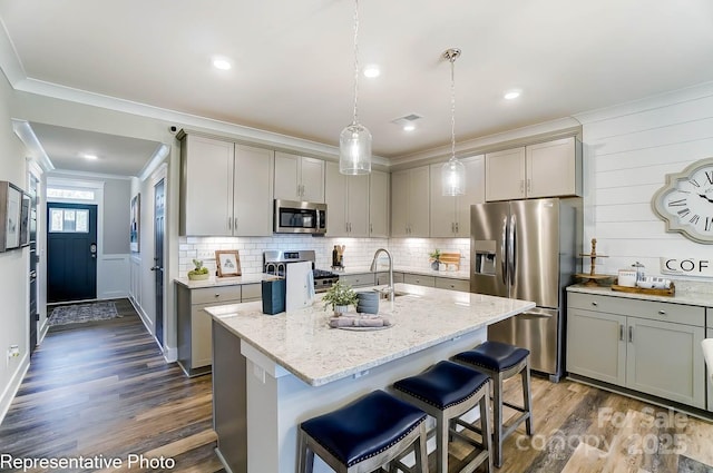 kitchen with crown molding, an island with sink, pendant lighting, stainless steel appliances, and light stone countertops