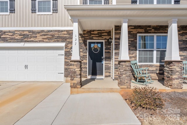 entrance to property with a garage, stone siding, covered porch, and board and batten siding