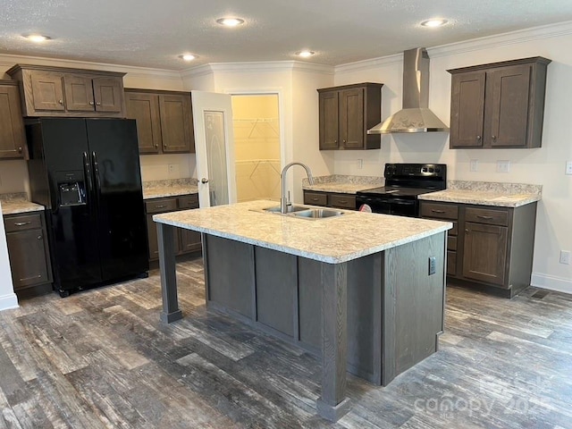 kitchen featuring light countertops, a kitchen island with sink, a sink, black appliances, and wall chimney exhaust hood