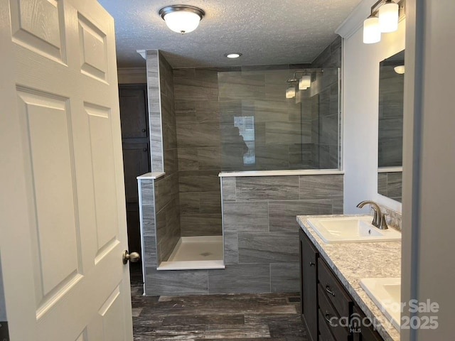 bathroom with double vanity, a sink, a textured ceiling, wood finished floors, and a walk in shower