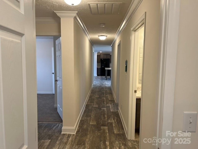 corridor featuring dark wood-style floors, visible vents, ornamental molding, a textured ceiling, and baseboards