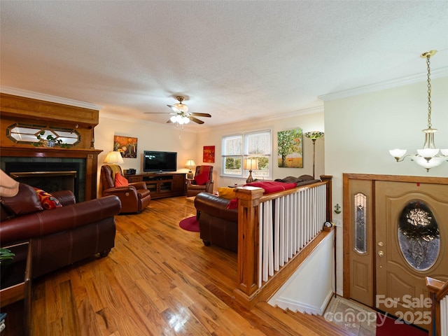 living room with a textured ceiling, a tile fireplace, ornamental molding, wood finished floors, and ceiling fan with notable chandelier