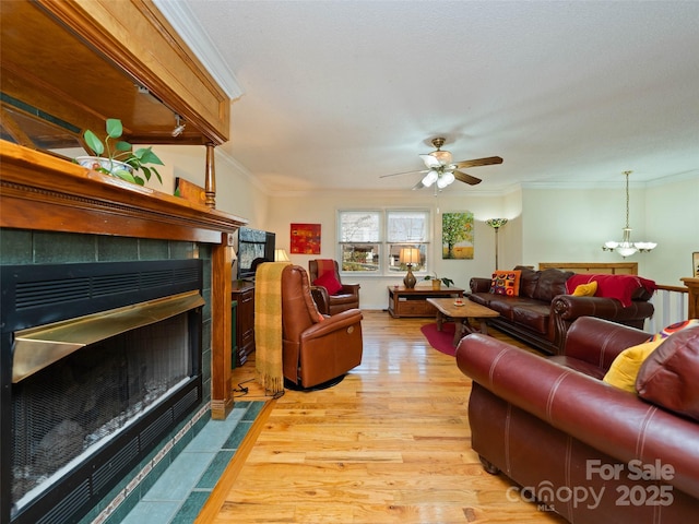 living room featuring light wood-style flooring, ornamental molding, ceiling fan with notable chandelier, and a fireplace