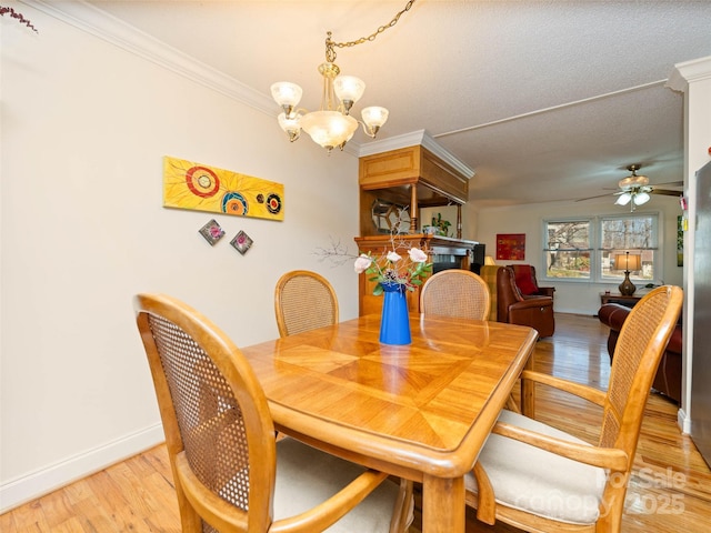 dining space with baseboards, light wood-style flooring, crown molding, and ceiling fan with notable chandelier