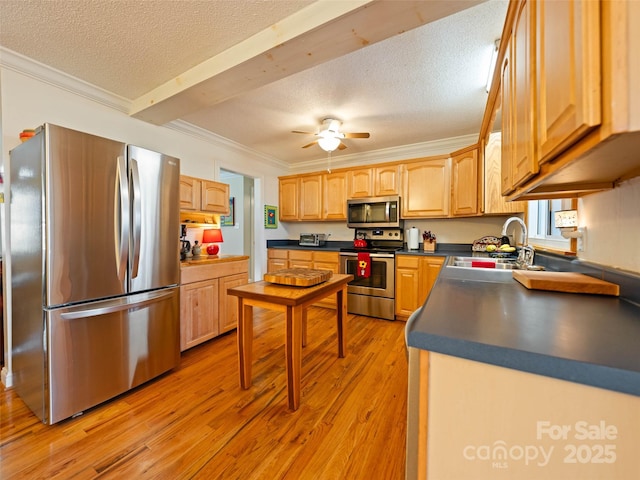 kitchen with ornamental molding, a sink, dark countertops, light wood-style floors, and appliances with stainless steel finishes