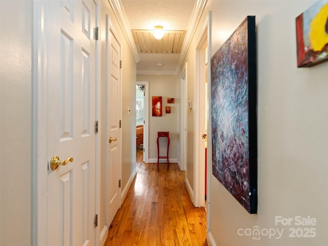 corridor featuring crown molding, light wood finished floors, attic access, a textured ceiling, and baseboards