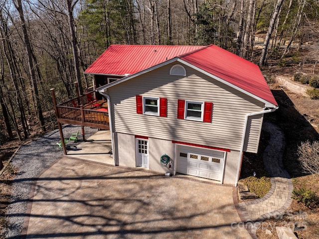 view of property exterior with driveway, a garage, metal roof, and a wooded view