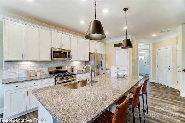 kitchen featuring sink, a kitchen island with sink, white cabinetry, stainless steel appliances, and decorative light fixtures