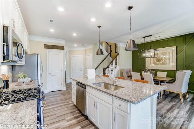 kitchen featuring sink, white cabinetry, appliances with stainless steel finishes, an island with sink, and pendant lighting