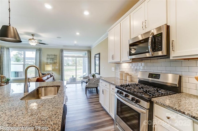 kitchen with appliances with stainless steel finishes, decorative light fixtures, white cabinetry, sink, and light stone countertops