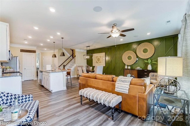 living room with ceiling fan, ornamental molding, sink, and light wood-type flooring