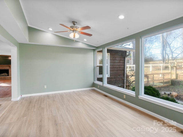 empty room featuring lofted ceiling, ornamental molding, ceiling fan, a brick fireplace, and light wood-type flooring