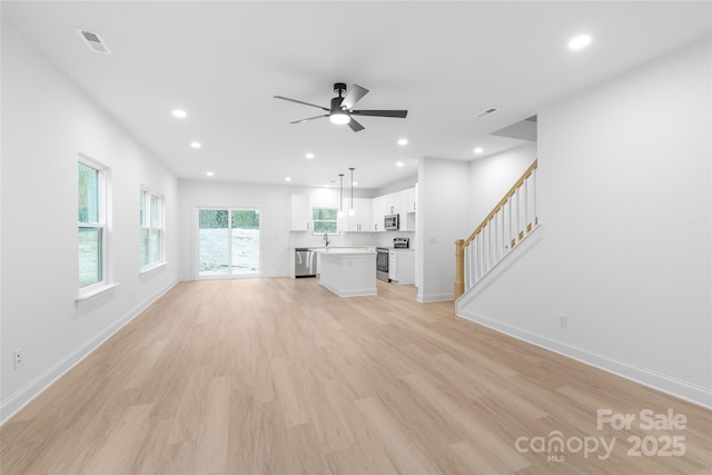 unfurnished living room with sink, ceiling fan, and light wood-type flooring