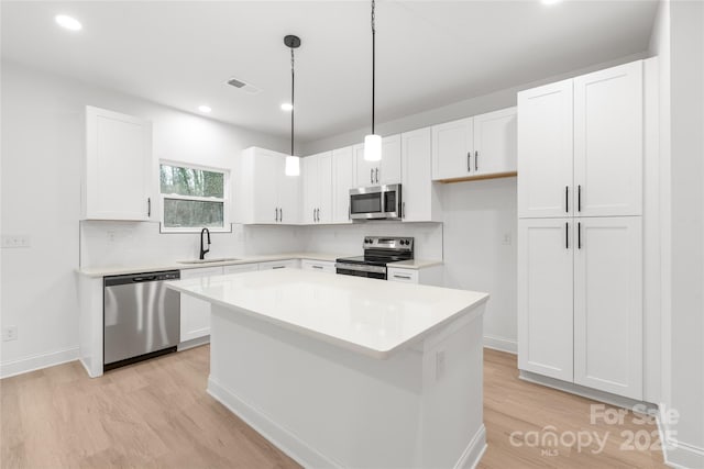 kitchen featuring stainless steel appliances, white cabinetry, a kitchen island, and sink