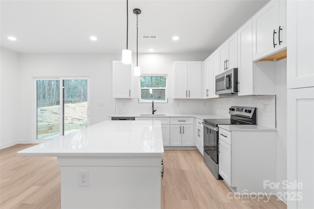 kitchen featuring sink, decorative light fixtures, a center island, stainless steel appliances, and white cabinets