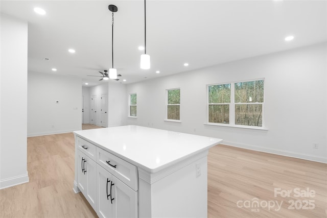 kitchen featuring light hardwood / wood-style flooring, ceiling fan, white cabinetry, hanging light fixtures, and a kitchen island