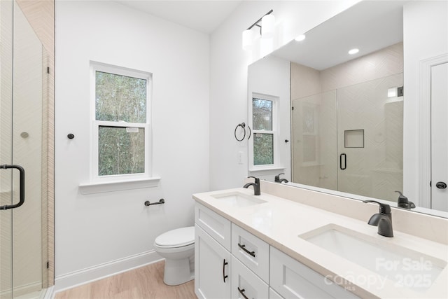 bathroom with wood-type flooring, a shower with shower door, vanity, and toilet