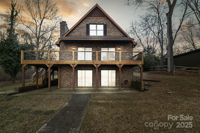 back house at dusk featuring a wooden deck, a yard, and a patio area