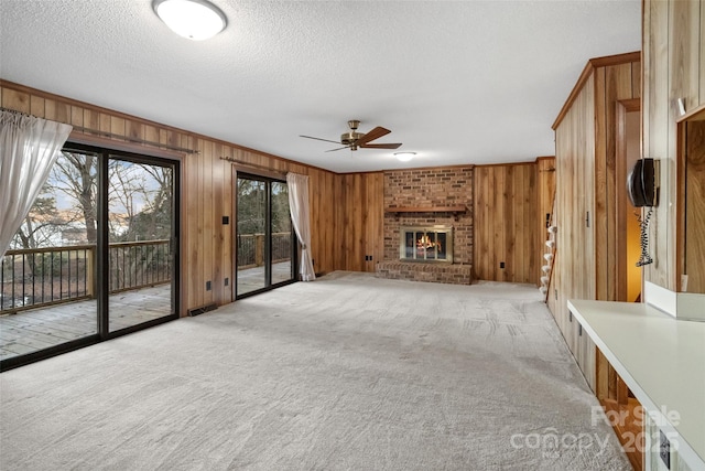 unfurnished living room with ceiling fan, a fireplace, a textured ceiling, light colored carpet, and wood walls