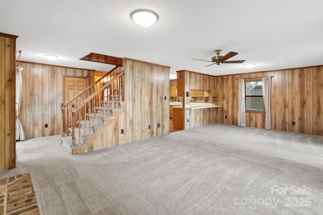 unfurnished living room with wood walls, carpet floors, ceiling fan, crown molding, and a textured ceiling