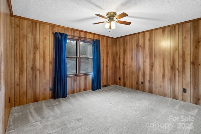 unfurnished room with wood walls, a textured ceiling, ornamental molding, carpet floors, and ceiling fan