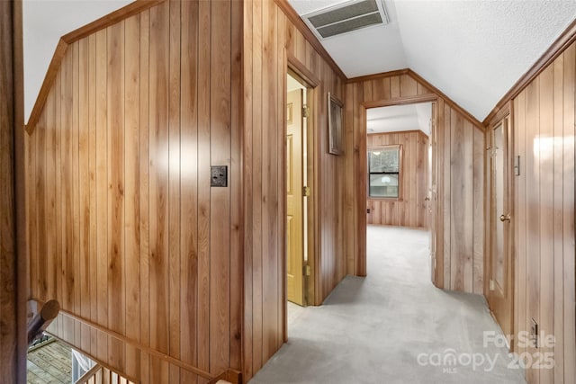 corridor featuring light colored carpet, wooden walls, and vaulted ceiling