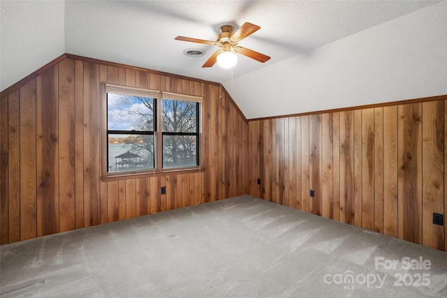 additional living space featuring vaulted ceiling, wooden walls, ceiling fan, and carpet