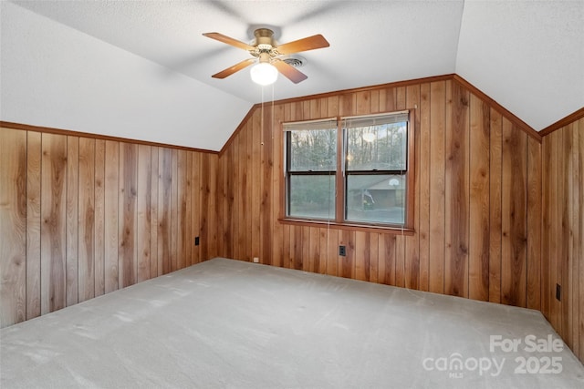 additional living space with lofted ceiling, ceiling fan, wooden walls, carpet, and a textured ceiling