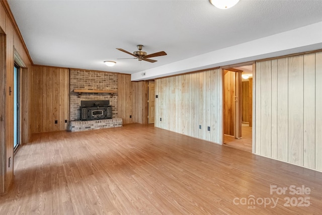 unfurnished living room with ceiling fan, wood-type flooring, wooden walls, and a wood stove