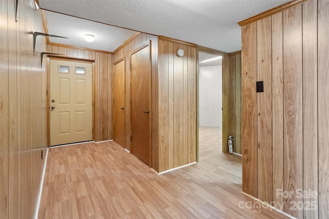 interior space with crown molding, wood walls, a textured ceiling, and light wood-type flooring