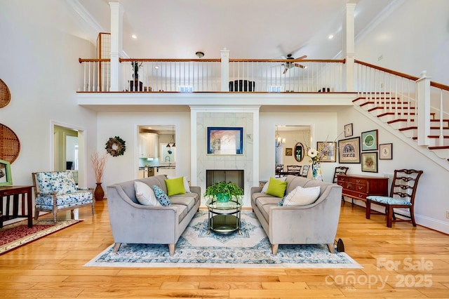 living room featuring ornamental molding, a towering ceiling, a fireplace, and light hardwood / wood-style flooring