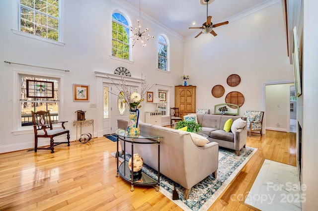 living room featuring a high ceiling, ornamental molding, ceiling fan with notable chandelier, and light hardwood / wood-style floors