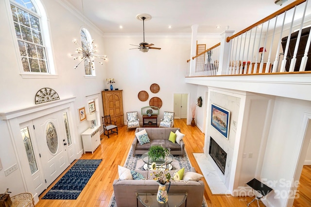 living room featuring a towering ceiling, ornamental molding, light hardwood / wood-style floors, and a notable chandelier