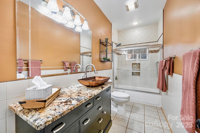 full bathroom with tile patterned floors, toilet, bath / shower combo with glass door, tile walls, and vanity