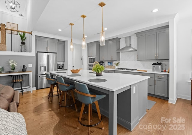 kitchen with gray cabinetry, appliances with stainless steel finishes, and wall chimney range hood