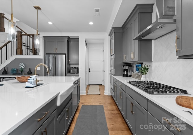 kitchen featuring pendant lighting, appliances with stainless steel finishes, gray cabinets, and wall chimney range hood