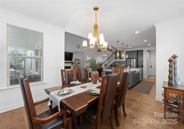 dining area with ornamental molding, an inviting chandelier, and light wood-type flooring